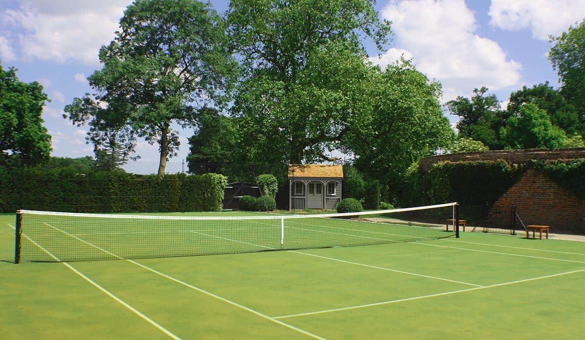 Mature trees fringe a tennis court built by En Tout Cas