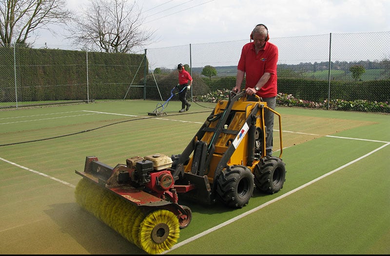 Brushing and cleaning a synthetic grass tennis court