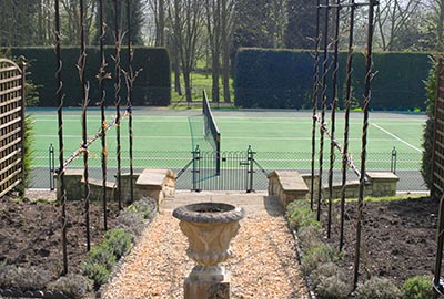 Tenis court fencing blends with garden landscaping